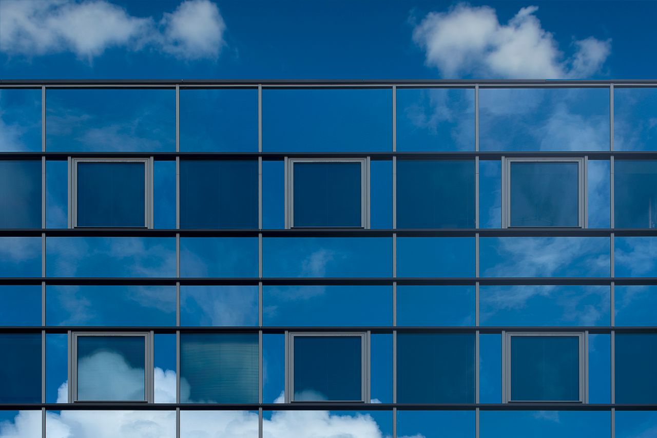 Facade of a modern glass building reflecting the blue sky and clouds.